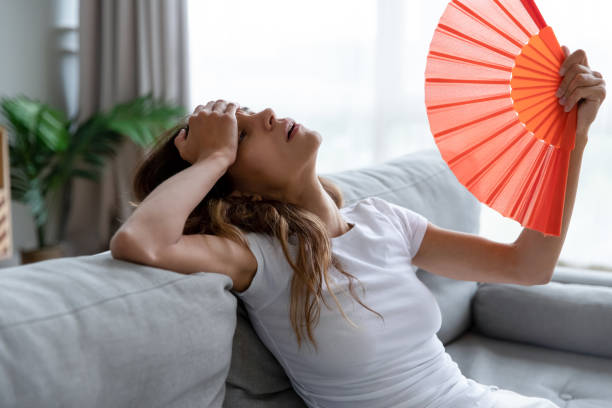 mujer con calor en casa usando abanico porque el aire acondicionado necesita reparación